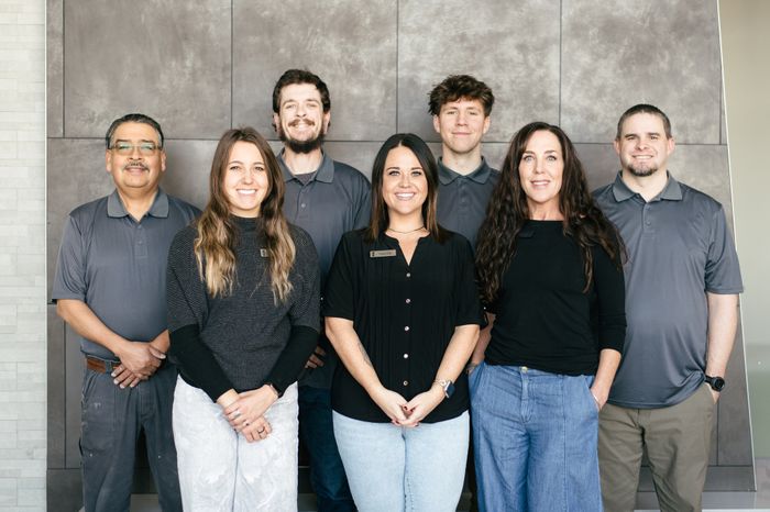 Friendly team posing together with smiles, dressed in coordinating attire against a modern, neutral backdrop.