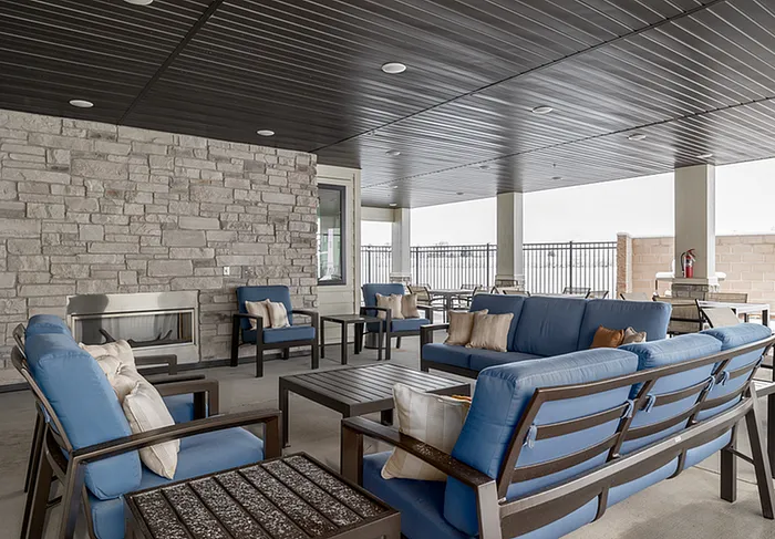 Inviting outdoor lounge area featuring stylish blue cushioned seating, a modern stone fireplace, and a sleek dark ceiling design.