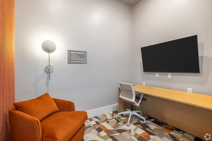 Modern study room with a sleek wall-mounted TV, cozy orange armchair, and a stylish workspace desk with ergonomic chair.