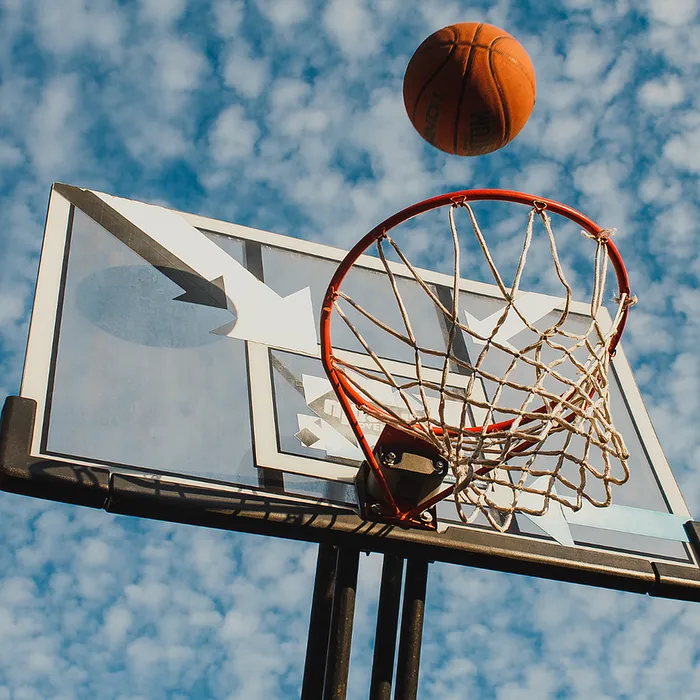 Dynamic basketball action with a ball soaring towards the hoop against a vibrant blue sky backdrop.