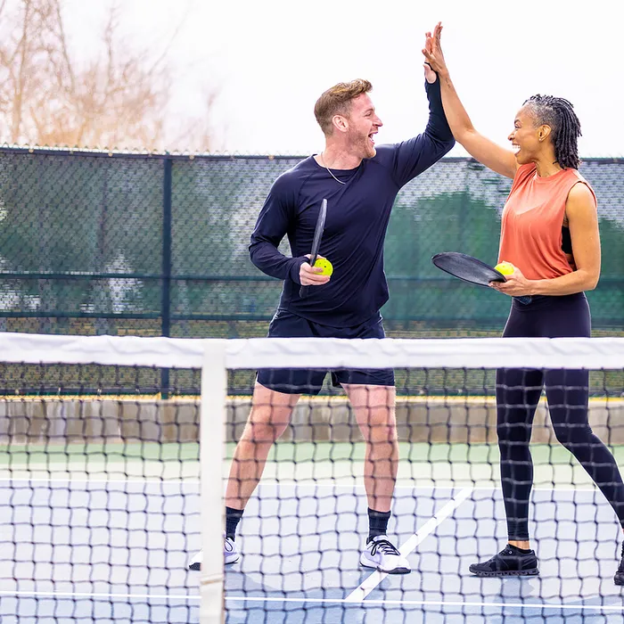 Energetic couple celebrating with a high-five on a pickleball court, holding paddles and a ball, showcasing a vibrant and active lifestyle.