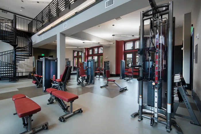 Modern fitness center with high-end gym equipment, featuring strength training machines and a stylish spiral staircase.