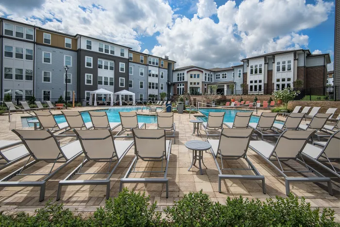Luxurious apartment complex with a sparkling outdoor pool, surrounded by comfortable lounge chairs and elegant cabanas, under a vibrant blue sky.