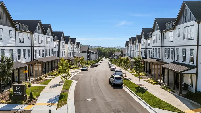 Charming suburban street lined with elegant townhomes, lush greenery, and clear blue skies.