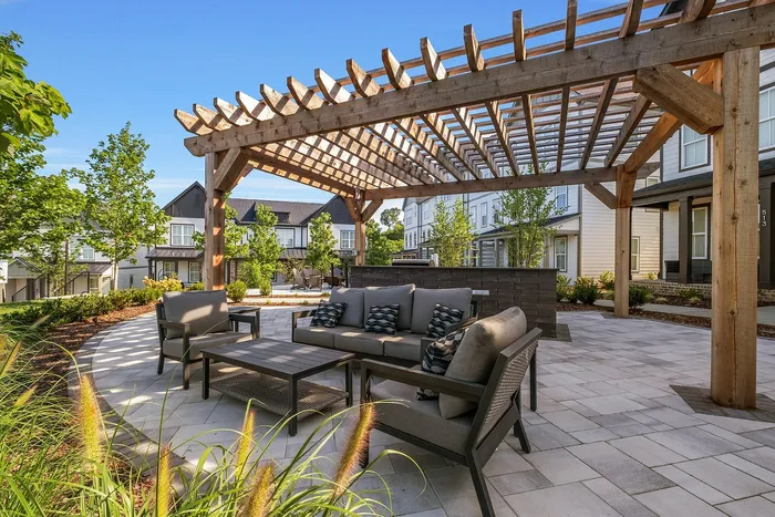 Charming outdoor patio with elegant wooden pergola and comfortable seating, surrounded by lush landscaping and modern townhouses.