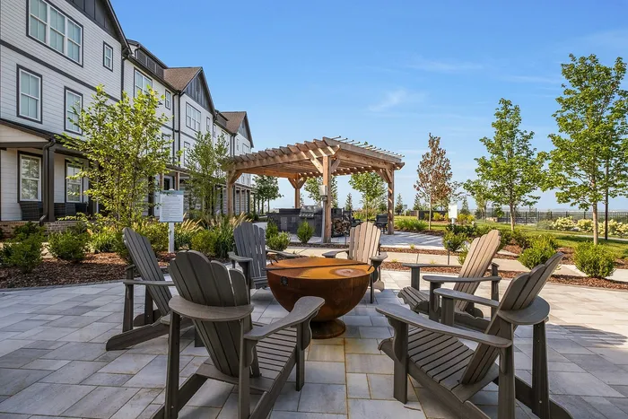 Charming outdoor patio with cozy Adirondack chairs around a stylish fire pit, adjacent to a pergola and lush landscaping.