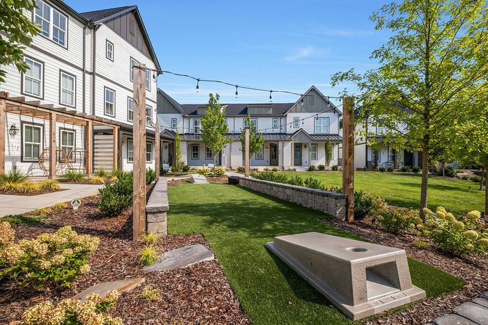 Modern apartment complex with elegant landscaping, featuring a communal outdoor area with a lawn and leisure space under clear blue skies.