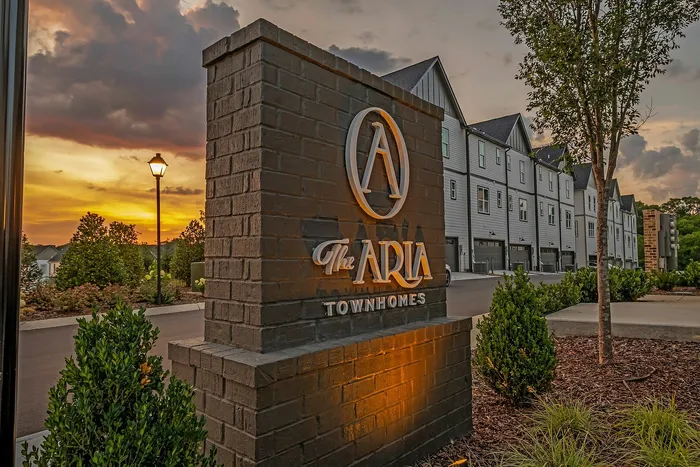 Elegant entrance to The Aria Townhomes, featuring modern architecture with charming evening ambiance and beautiful landscaping.