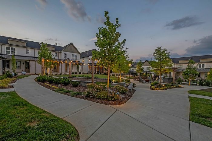 Charming twilight view of a picturesque apartment complex with elegant landscaping, patio string lights, and inviting walkways.