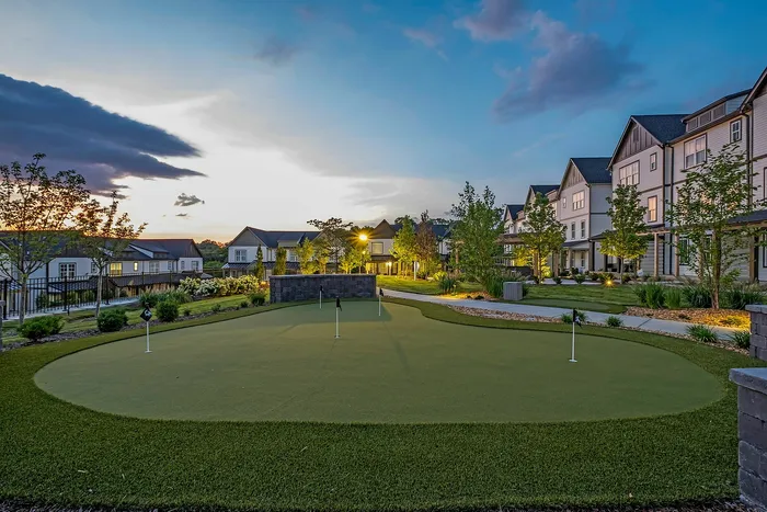 Charming residential community at dusk featuring well-manicured grounds and a modern putting green, surrounded by elegant multi-story homes.