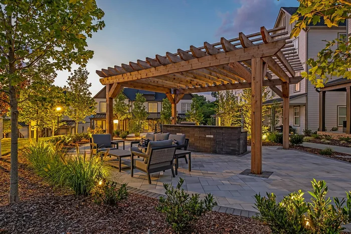 Charming outdoor patio with stylish wooden pergola and cozy seating, surrounded by lush greenery and warm evening lighting.