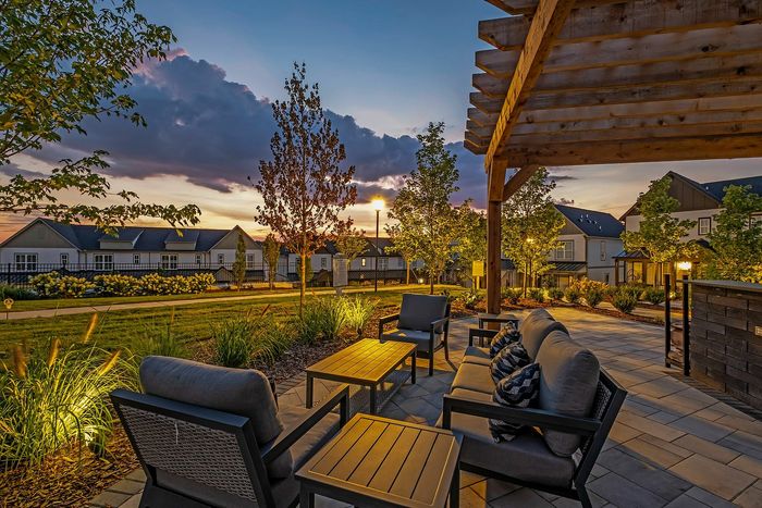 Charming patio area with cozy outdoor seating, overlooking a picturesque sunset and beautifully landscaped garden.
