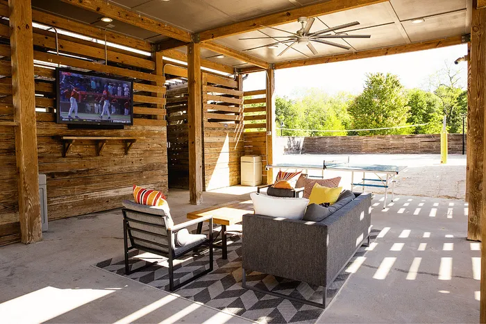 Covered outdoor lounge with seating, TV, ping pong table and sand volleyball court at Wildwood Baton Rouge student apartments near LSU