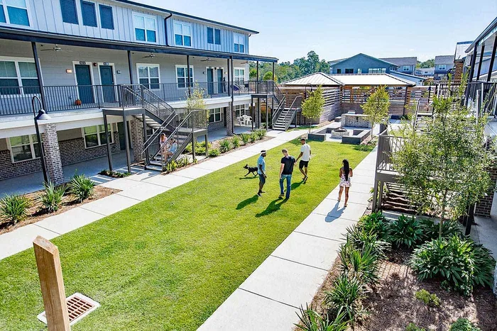 Students walking across courtyard lawn with fire pit and seating at Wildwood Baton Rouge student apartments near LSU
