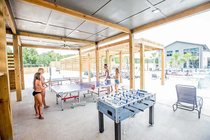 Students playing ping pong and foosball in covered outdoor game lounge at Wildwood Baton Rouge apartments near LSU