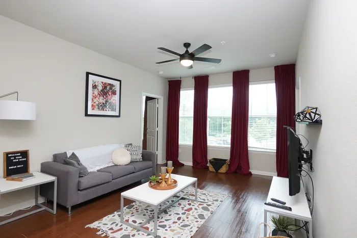 Cozy living room with modern gray sofa, stylish art, and large windows with elegant red curtains.