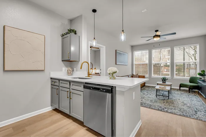 Modern kitchen and living space with sleek grey cabinetry, elegant lighting, and an open-concept design featuring a cozy living room with abundant natural light.