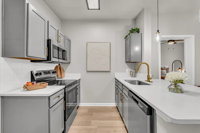 Modern kitchen with sleek gray cabinetry, stainless steel appliances, and elegant gold fixtures. Spacious countertop adorned with flowers for a touch of sophistication.