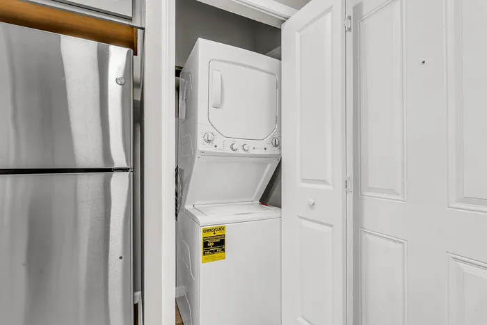 Efficient in-unit laundry with a sleek stackable washer and dryer next to a modern stainless steel refrigerator, offering convenience and style.