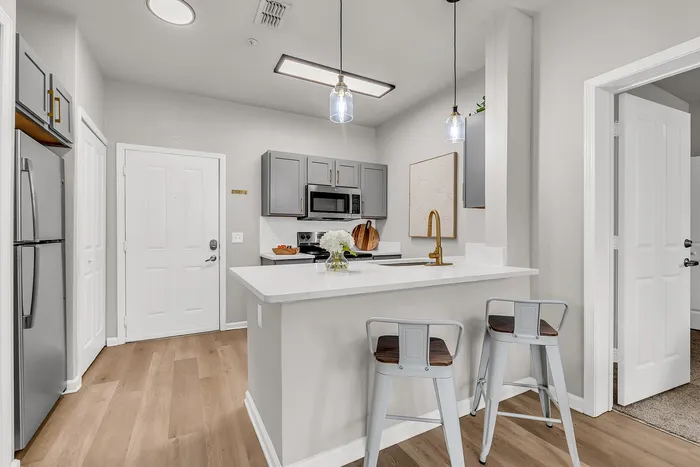 Modern kitchen with sleek gray cabinetry, elegant pendant lighting, and a stylish breakfast bar with stools, offering a perfect blend of functionality and design.