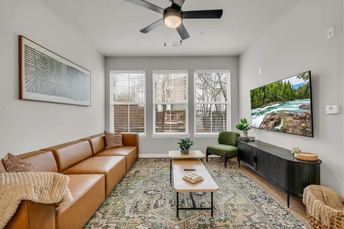 Bright and inviting living room featuring a chic brown leather sofa, contemporary artwork, and a large wall-mounted TV showcasing a stunning nature scene, accented by a stylish area rug and greenery.