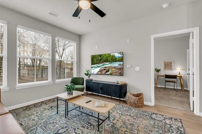Cozy living room with large windows, stylish decor, and an adjoining office space, filled with natural light and modern furnishings.