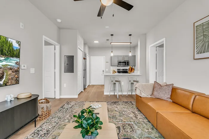 Chic modern living area with a cozy leather sofa, stylish rug, and open-concept kitchen with sleek barstools under pendant lighting.