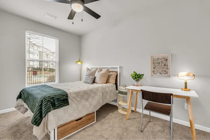 Bright and cozy bedroom with modern decor, featuring a sleek desk, plush bed, and large window offering abundant natural light.