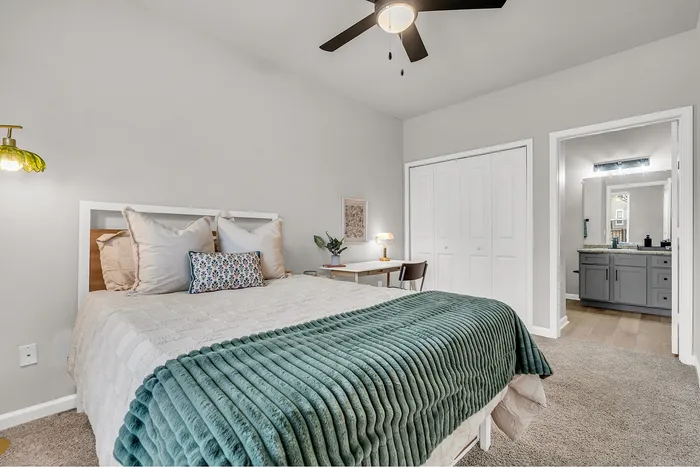 Elegant bedroom with plush bedding, cozy carpet, and a sleek ceiling fan, featuring a stylish workspace and a modern en-suite bathroom.