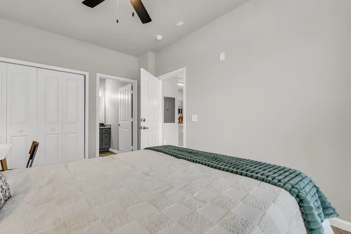 Inviting bedroom with cozy bedding, sleek ceiling fan, and access to a modern bathroom.