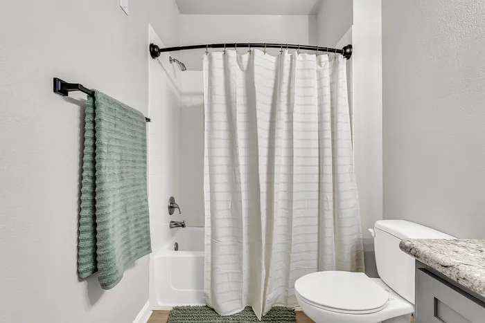 Modern bathroom featuring elegant white tile shower, soft green accents, and luxurious granite countertop.