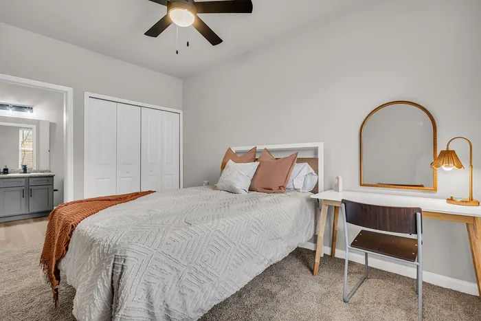 Cozy bedroom with modern ceiling fan, stylish bed with earth-toned pillows, and elegant desk with warm lighting.