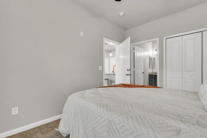 Elegant bedroom with cozy textured bedding, adjoining modern bathroom, and ample closet space.