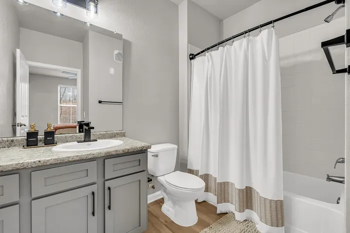 Modern bathroom featuring sleek grey cabinetry, elegant countertop with stylish faucet, and a cozy bathtub with a classic white shower curtain.