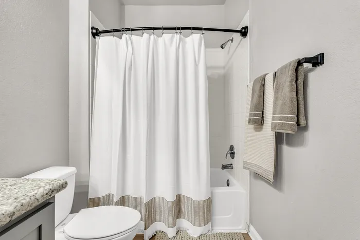 Modern bathroom featuring a sleek countertop, elegant white shower curtain, and coordinated towel set for a cozy and stylish appeal.