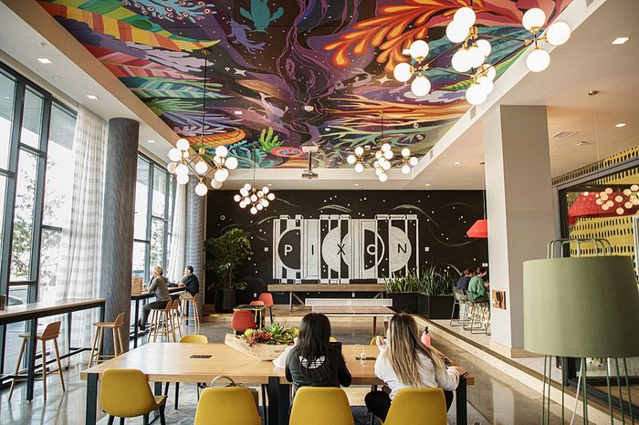 Vibrant communal space featuring colorful ceiling art, chic lighting, and large windows offering natural light.
