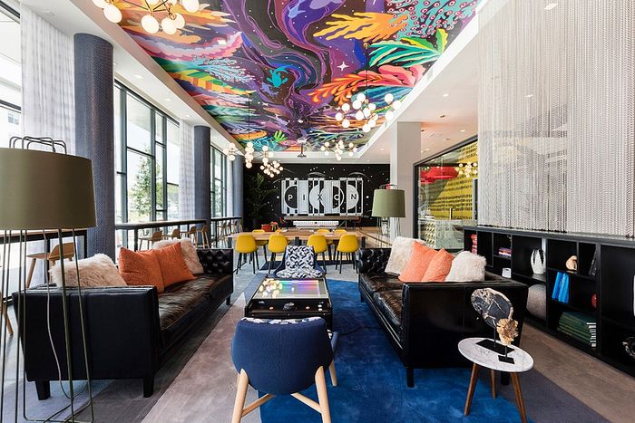 Vibrant modern apartment lounge featuring bold artwork on the ceiling, stylish seating, and extensive natural lighting.