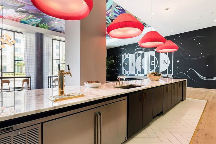 Modern communal workspace with sleek marble countertops, vibrant red pendant lights, and artistic wall mural.
