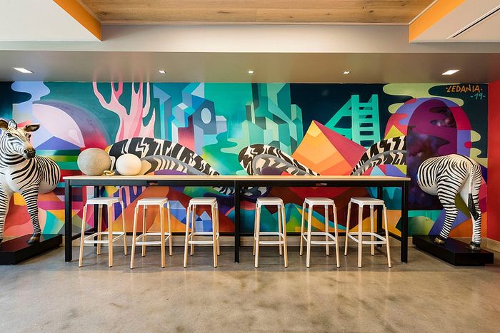 Vibrant dining area with a striking mural featuring geometric shapes and zebras, complemented by a sleek row of modern bar stools.