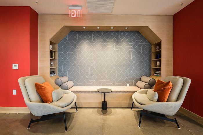 Modern seating area with stylish geometric wall design, cozy lounge chairs with vibrant cushions, and warm wooden accents.