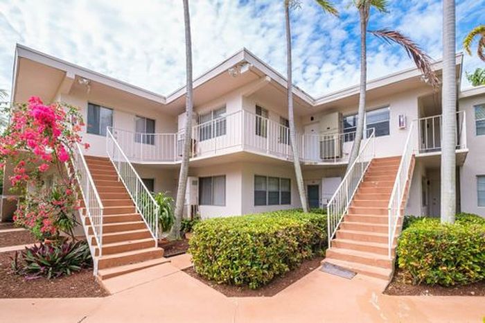 Charming apartment complex with lush landscaping and vibrant pink flowers, featuring dual staircases leading to second-floor units.