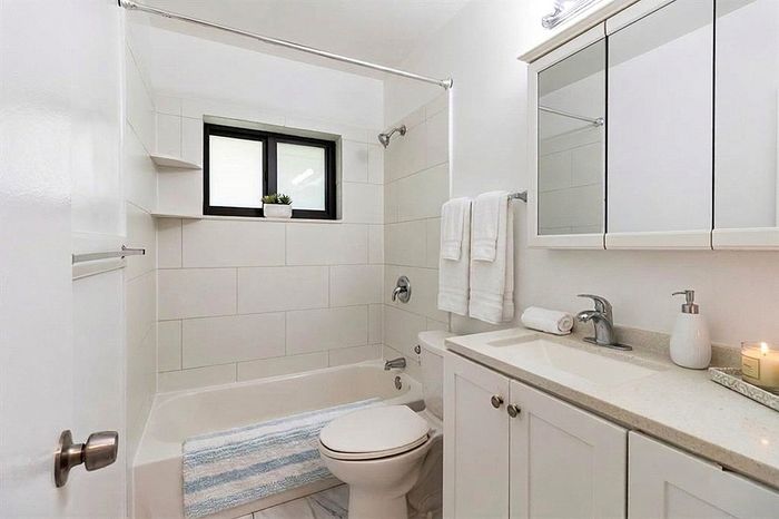 Elegant bathroom with pristine white tiles, modern fixtures, and cozy ambiance, showcasing a relaxing bathtub and ample storage.
