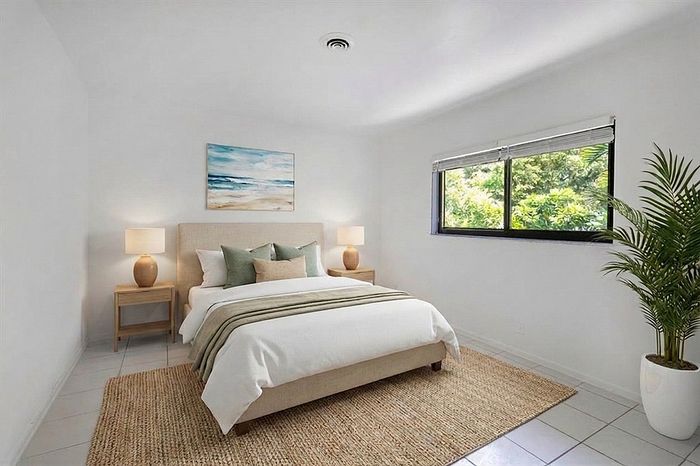 Bright and airy bedroom featuring a cozy bed with elegant pillows, large window with lush green views, and stylish decor for a tranquil living space.