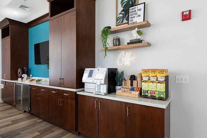 Modern coffee station with sleek wooden cabinets, trendy decor, and a variety of brewing options for a warm, inviting atmosphere.
