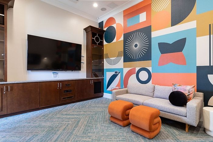 Vibrant living room with modern geometric wall art, cozy grey sofa, and stylish orange ottomans complementing the sleek entertainment center.