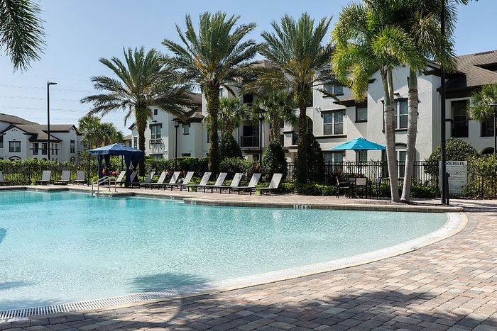 Inviting resort-style pool area surrounded by lush palm trees and elegant apartment buildings, perfect for relaxation and leisure.