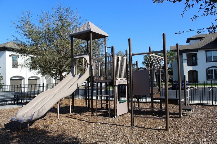 Family-friendly apartment complex featuring a modern playground with slides and climbing structures, surrounded by lush greenery and spacious outdoor areas.