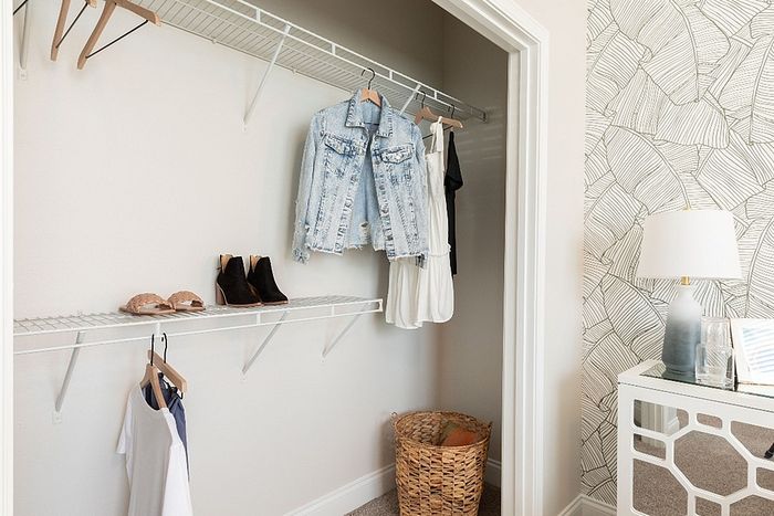 Chic closet with denim jacket, stylish shoes, and a sleek modern lamp on a patterned wallpaper backdrop.