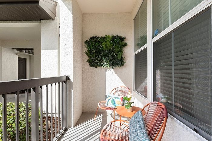 Inviting apartment balcony with cozy seating, vibrant cushions, and lush greenery, bathed in sunlight for a relaxing outdoor retreat.