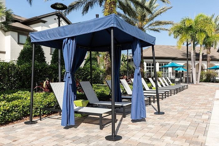 Luxurious poolside cabana with elegant blue drapes, surrounded by stylish lounge chairs and tropical palm trees, offering a serene escape.